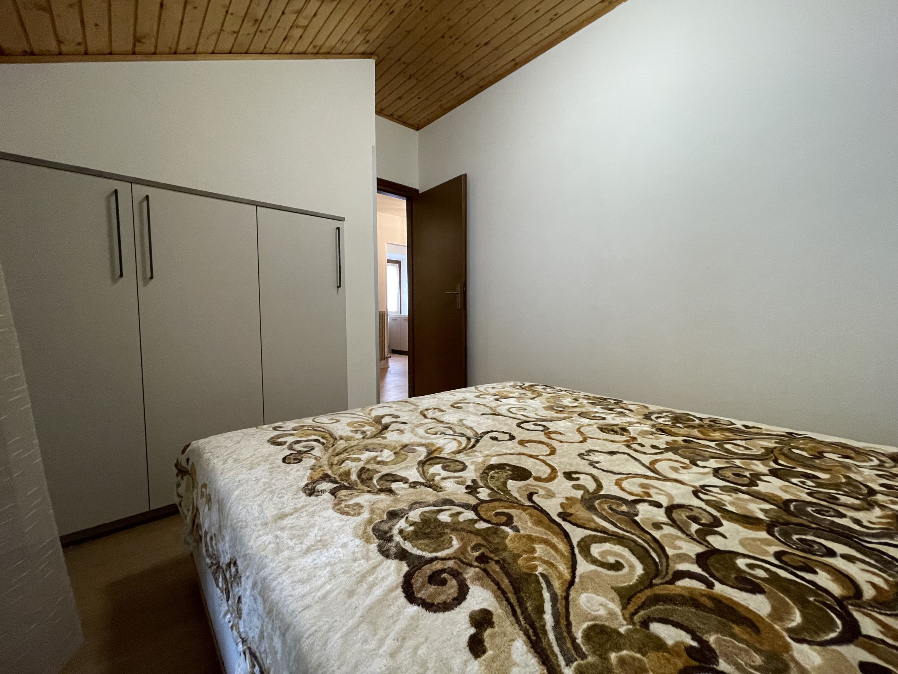 A bedroom with a bed, a wardrobe, and a wooden ceiling.