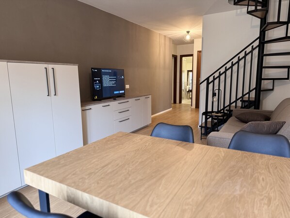 Une cuisine moderne avec des meubles blancs, une table à manger en bois et un téléviseur encastré qui affiche un menu.