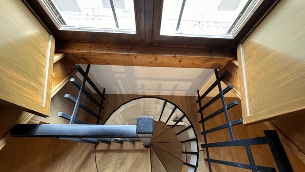 Una escalera de caracol con tragaluz superior, paredes de madera y barandales de metal.