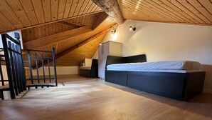 Un dormitorio tipo loft con techo inclinado, piso de madera, una cama, un escritorio y una escalera.