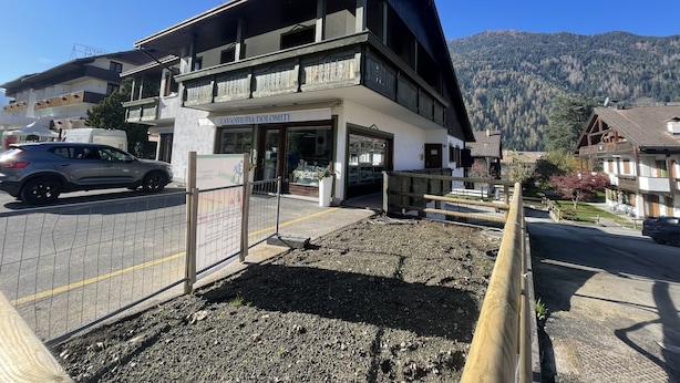 A two-story building with a balcony, a sign reading "LAVANDERIA DOLOMITI," and a mountainous backdrop.