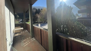 A covered balcony with a view of a parking area and trees.