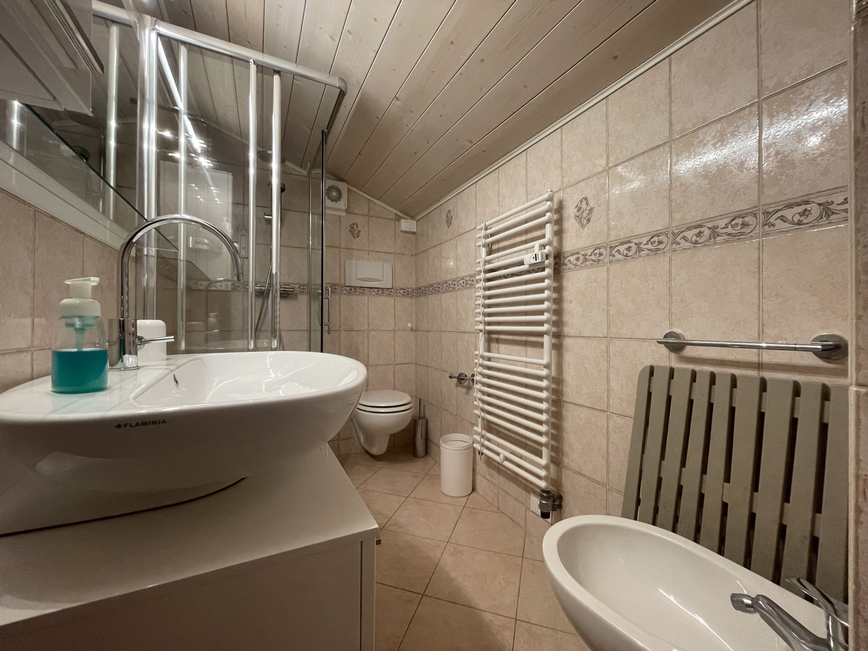 A bathroom with a large sink, a mirror, a shower, a toilet, and a radiator.