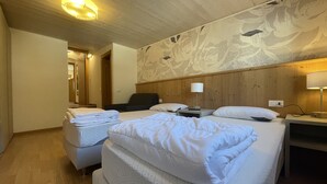 A hotel room with two beds, a wooden headboard, a nightstand, a lamp, and a wall with a floral pattern.