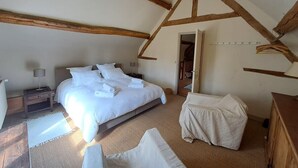 A bedroom with a large bed, a bedside table, a chair, and a wooden ceiling structure.