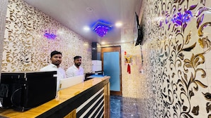 A reception area with ornate wallpaper, a reception desk, and a television mounted on the wall. - Welcome Star (Mumbai)