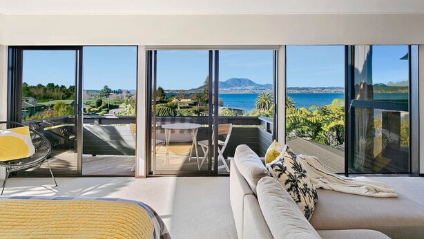 A modern living room with large windows, a sofa, a dining table, and a chair.