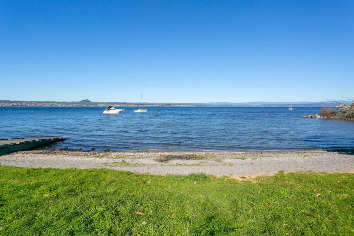 A clear view of a lake with boats, a grassy shore, and a distant mountain range.