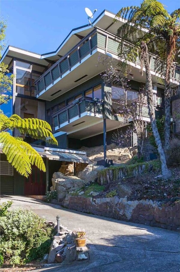 Un edificio moderno de varios pisos con balcones, rodeado de vegetación y un paisaje rocoso.