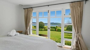 A bedroom with a large bed, a view of a well-manicured garden, and a door leading outside.