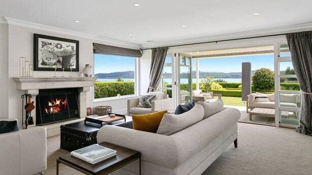 A modern living room with a fireplace, a sofa, a coffee table, and a view of a landscaped garden through large glass doors.
