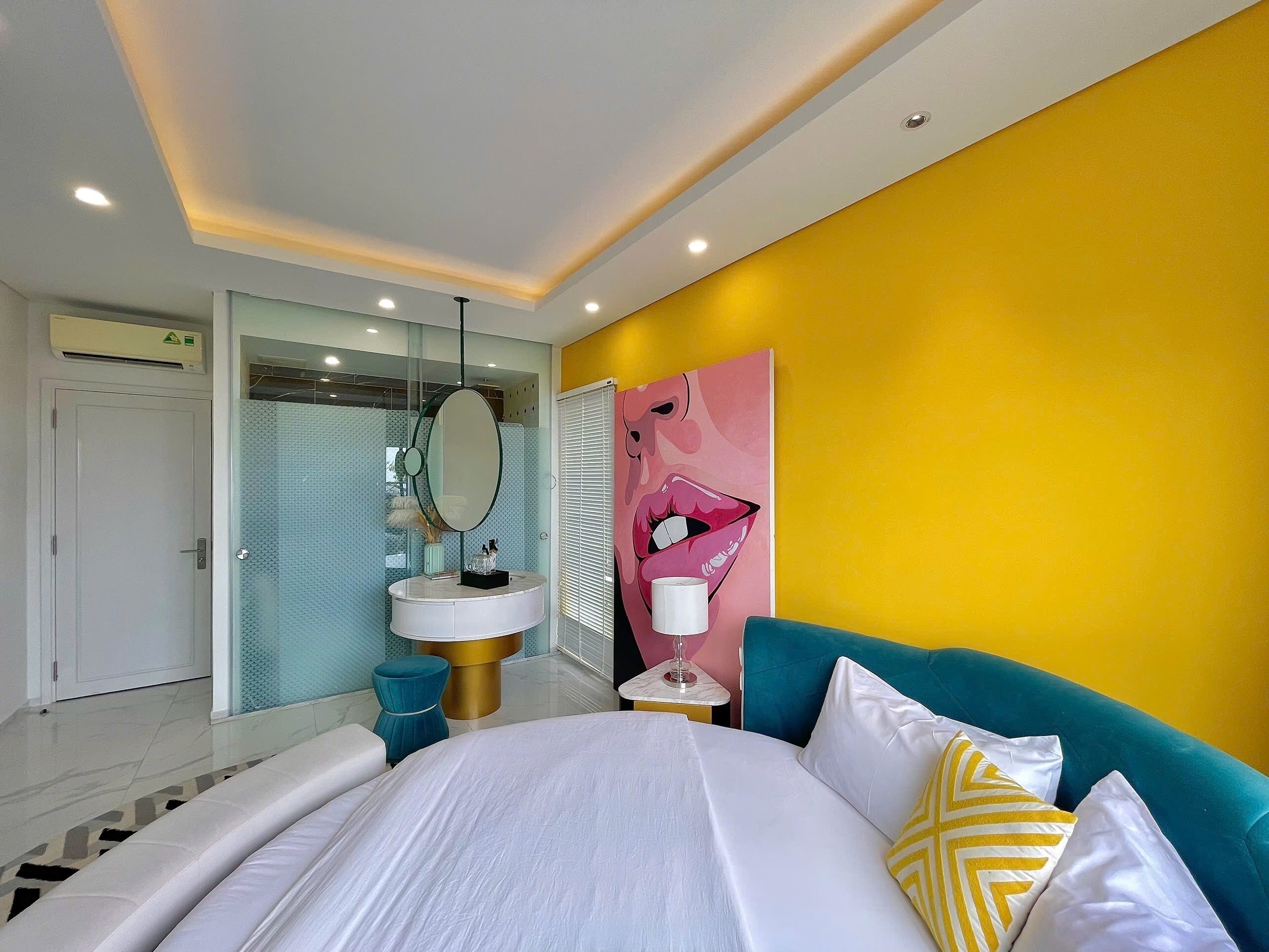 A modern hotel room with a large bed, a round mirror, a sink, and a vibrant yellow accent wall.