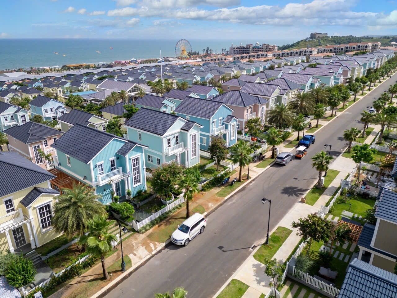 A coastal residential area with rows of houses, a road, and a distant view of a beach and a large Ferris wheel.