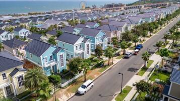 A coastal residential area with rows of houses, a road, and a distant view of a beach and a large Ferris wheel.