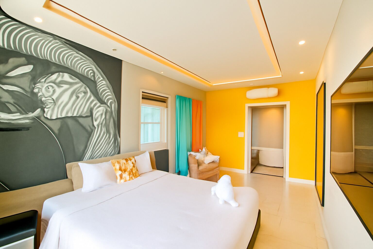 Una habitación de hotel moderna con una cama grande, un baño con inodoro y lavamanos, y un pasillo que conduce a otra habitación.
