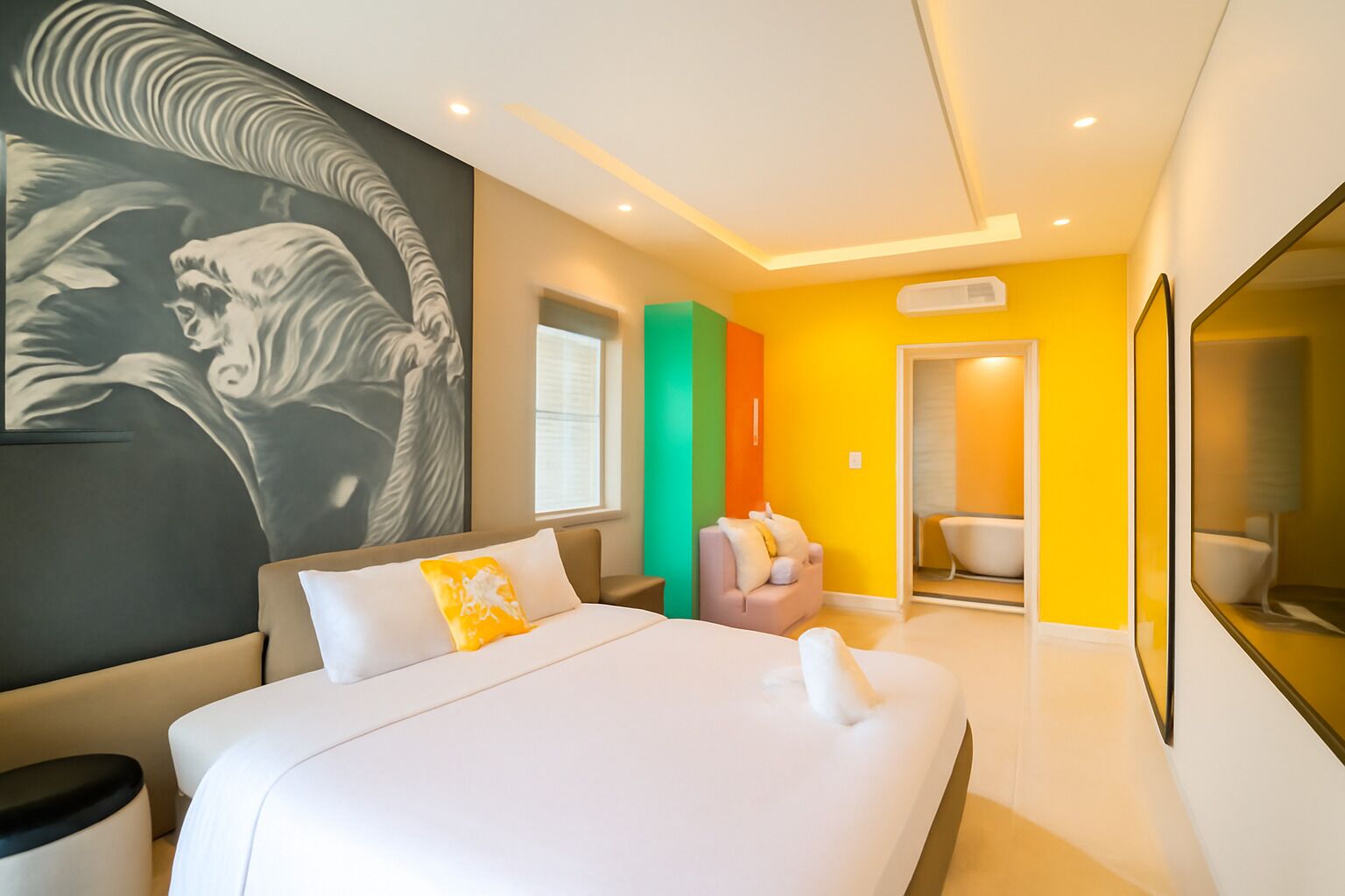 Een moderne hotelkamer met een groot bed, een zithoek met een bank, een badkamer met een bad, en een grote spiegel.