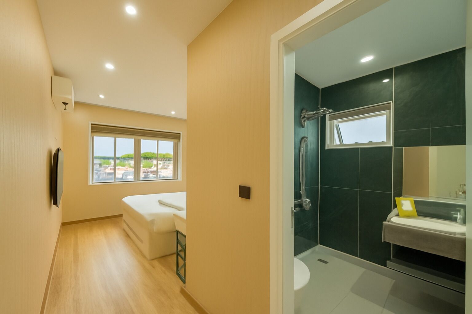 A hotel room with a bed, a window with a view, a shower area, and a toilet.