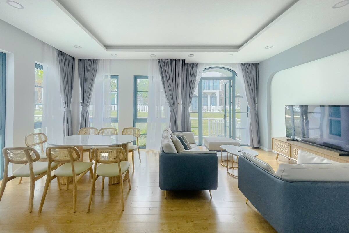 A modern living room with a dining area, large windows, and a flat-screen TV.