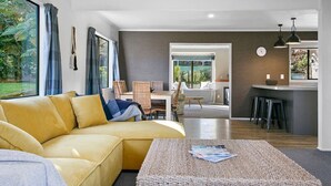 Ein modernes Wohnzimmer mit einem gelben Sofa, einem Couchtisch und Blick auf den Garten durch große Fenster.