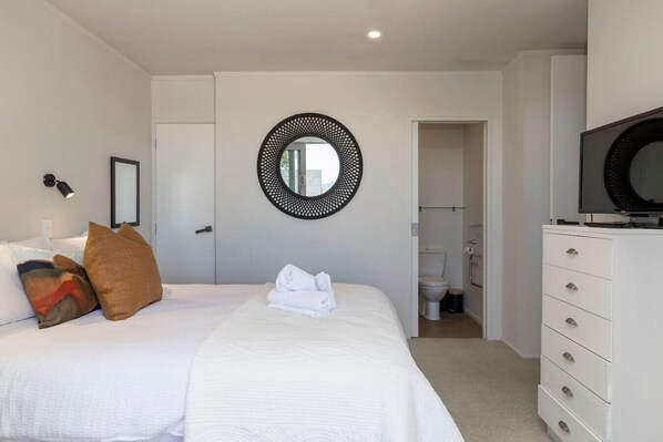 Ein Hotelzimmer mit Bett, einem runden Spiegel, einem Fernseher und einem durchgegangenen Tür angedeuteten Badezimmer.