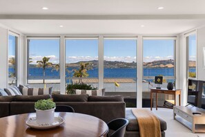 Ein modernes Wohnzimmer mit großem Fenster mit Blick auf ein Gewässer und Hügel.