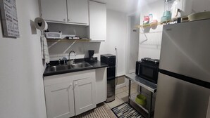 A compact kitchen with white cabinets, a black countertop, a sink, a coffee maker, a microwave, and a refrigerator.
