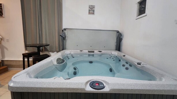 A hot tub with a control panel, a small table, and a window in a room with white walls.