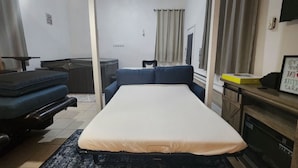 A bedroom with a bed, a desk, a chair, and a small table.