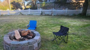 A backyard with a stone fire pit, two black folding chairs, and a blue folding chair.