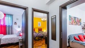 Ein modernes Hotelzimmer mit Holzboden, einem Bett mit floralem Bettzeug, einer Couch mit roten Kissen und einem großen, abstrakten Gemälde an der Wand.