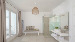 A modern bathroom with a glass shower, a white bench, and a large mirror. - Hilas suites (Imerovigli)
