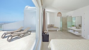 A modern bedroom with a large bed, a glass-enclosed shower, a seating area with a bench, and a balcony with sun loungers. - Hilas suites (Imerovigli)