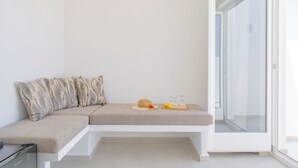 A modern room with a built-in bench, a glass door, and a small table with a hat and lemons. - Hilas suites (Imerovigli)