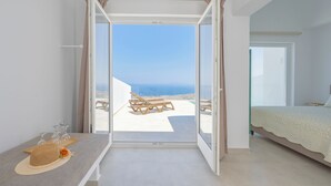 A bedroom with a large sliding glass door leading to a balcony with a view of the sea. - Hilas suites (Imerovigli)