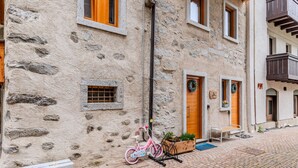 A stone building with wooden shutters, a bicycle, and a bench outside.