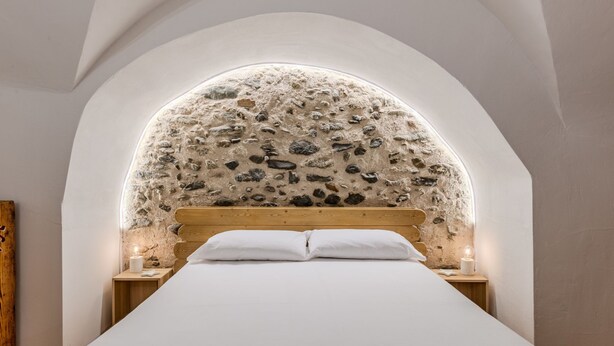A bedroom with a stone wall arch, a wooden bed frame, and a white bedspread.