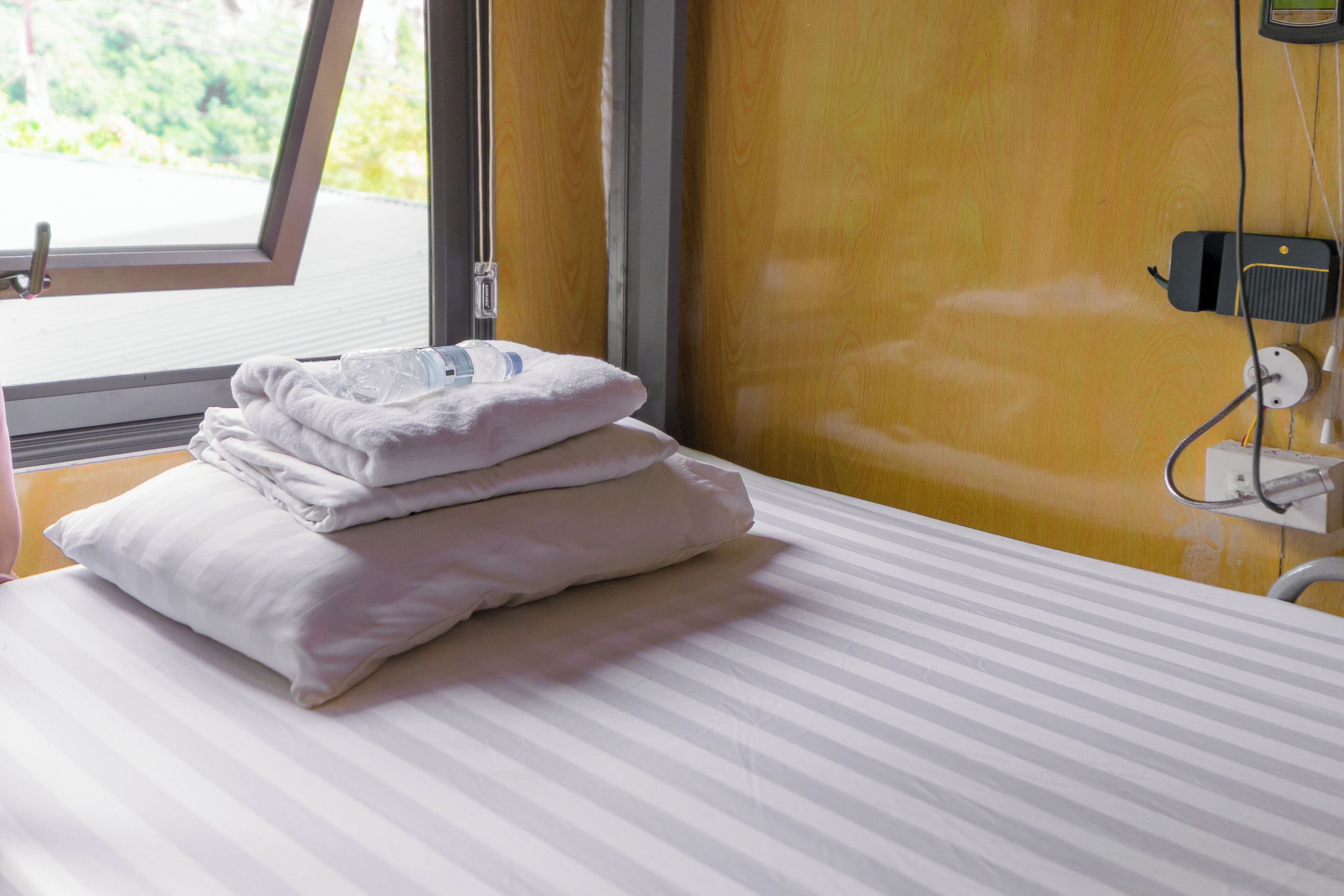 Une chambre d’hôtel avec un lit, des oreillers, une fenêtre et une table de chevet équipée d’une prise électrique et d’un appareil.