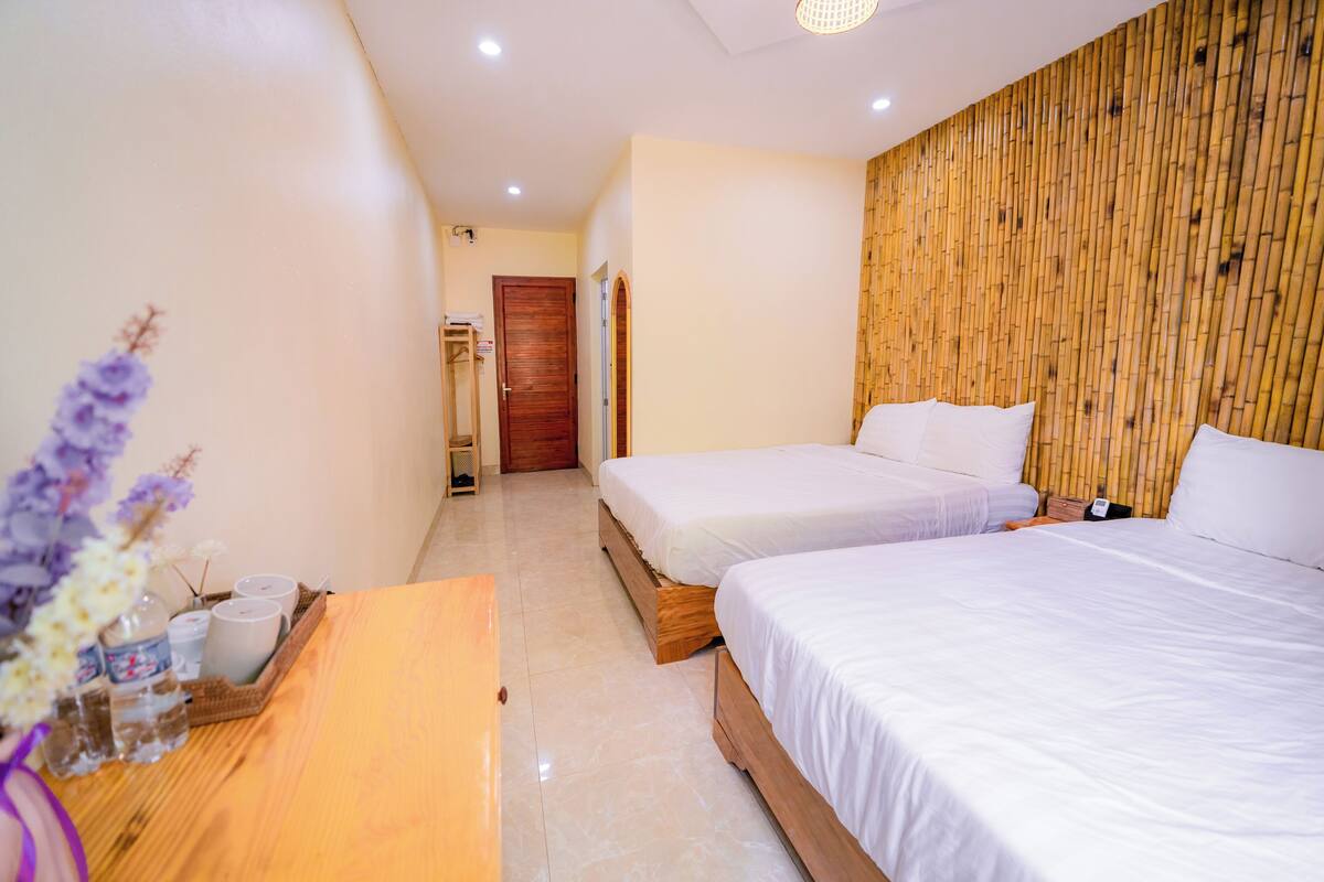 A hotel room with two beds, a wooden headboard, a wooden desk with a vase of flowers, and a wooden wardrobe.