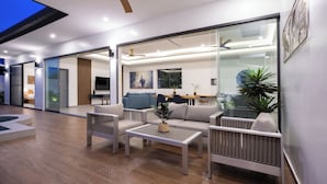 A modern living room with a sofa, coffee table, and chairs, a dining area with a table and chairs, and a kitchen visible through glass doors. - Two-Bedroom Villa with Salt Pool in Rawai (rawai)