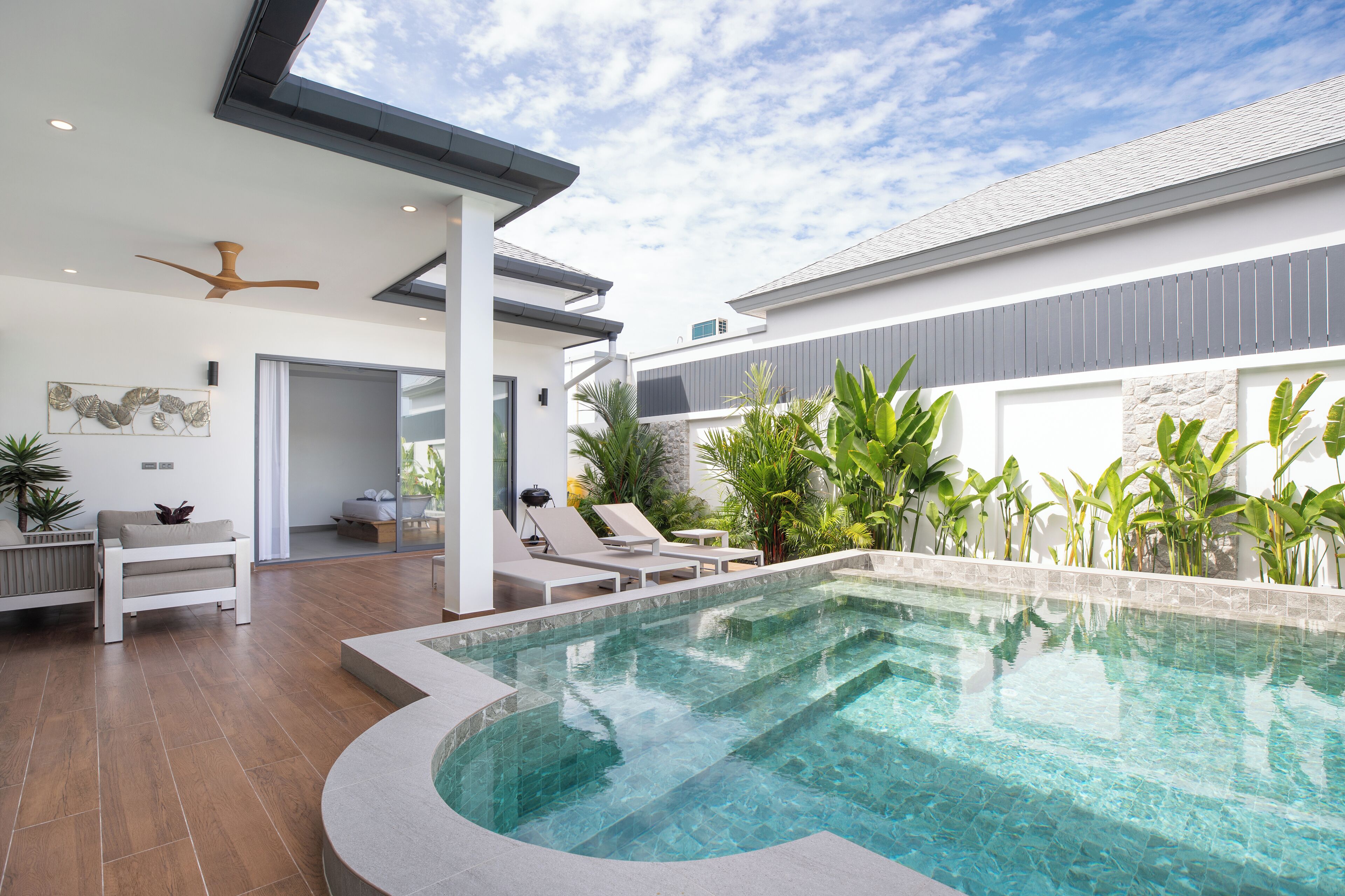 Ein moderner Außenpoolbereich mit Pool in gebogener Form, Liegestühlen und Deckenventilator.