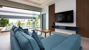 A modern living room with a large flat-screen TV, a wooden coffee table, and a blue sofa. - Two-Bedroom Villa with Salt Pool in Rawai (rawai)