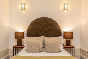 A neatly made bed with a large, round headboard, flanked by two bedside lamps on matching nightstands. - Modern Porto studio with essential amenities (Oporto)