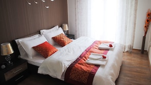 A neatly made bed with white and red bedding, a bedside lamp, and a vase with flowers on the nightstand. - Athens Comfortable Stay Apartment (Athens)