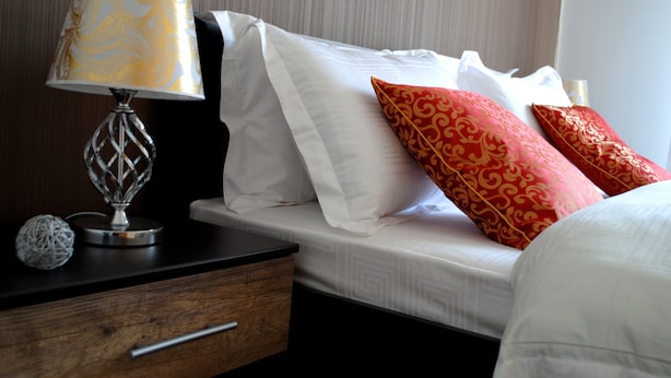 A neatly made bed with white and red patterned pillows, a bedside table with a lamp, and a decorative sphere on the nightstand. - Athens Comfortable Stay Apartment (Athens)