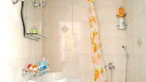 A bathroom with a white sink, a shower with a patterned curtain, and a shelf with toiletries. - Athens Comfortable Stay Apartment (Athens)