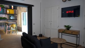 Un salon moderne avec un canapé noir, une table basse ronde en bois et un téléviseur fixé au mur qui affiche le logo de Netflix.