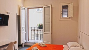 Une chambre d’hôtel avec un lit, un bureau, une chaise et un téléviseur fixé au mur.
