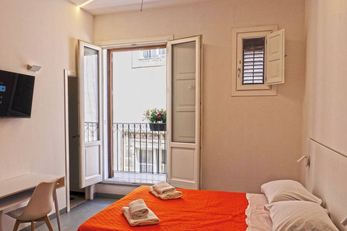 Quarto de hotel com uma cama, escrivaninha, cadeira e televisão na parede.