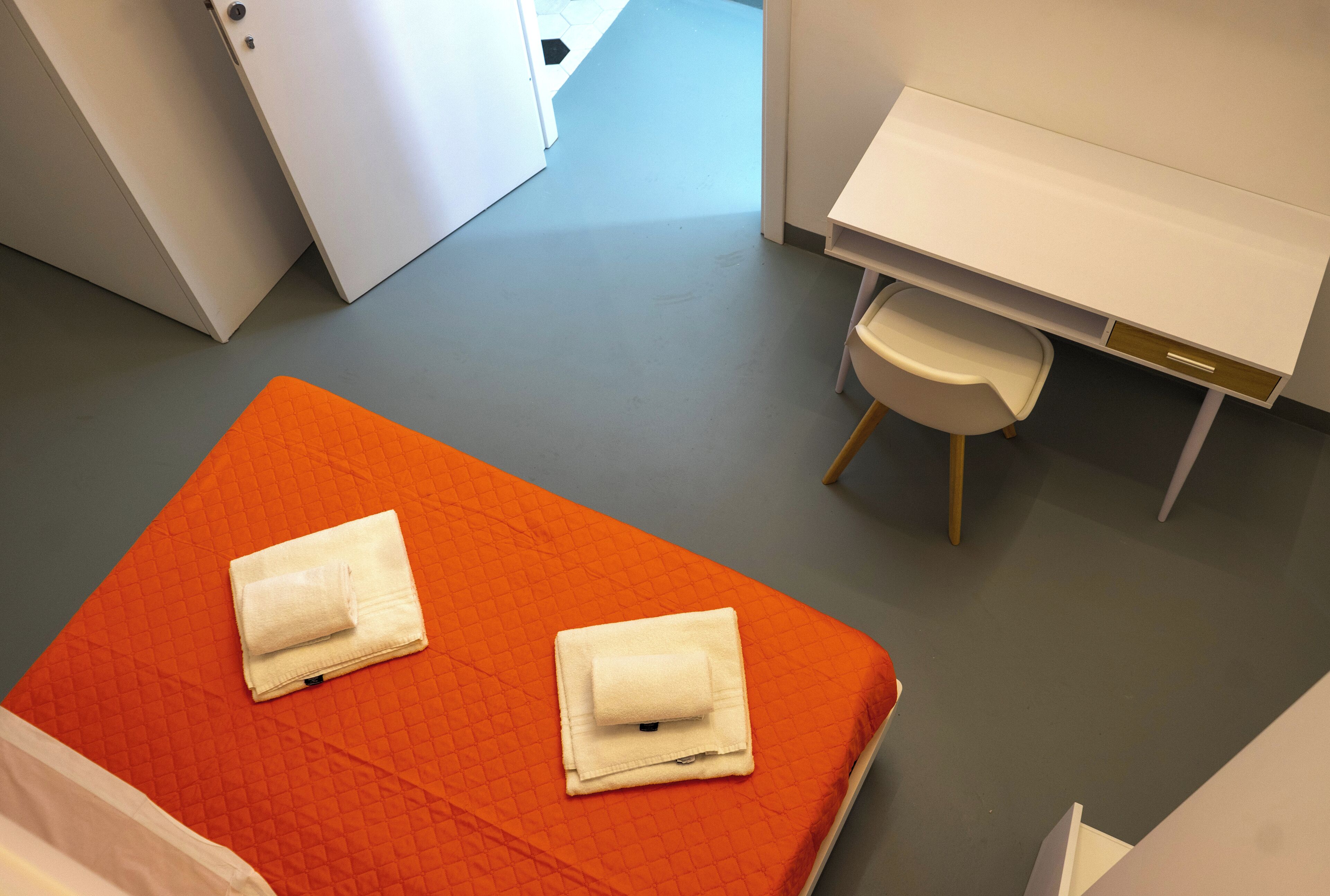 Una habitación de hotel con una cama naranja, un escritorio blanco y una silla.