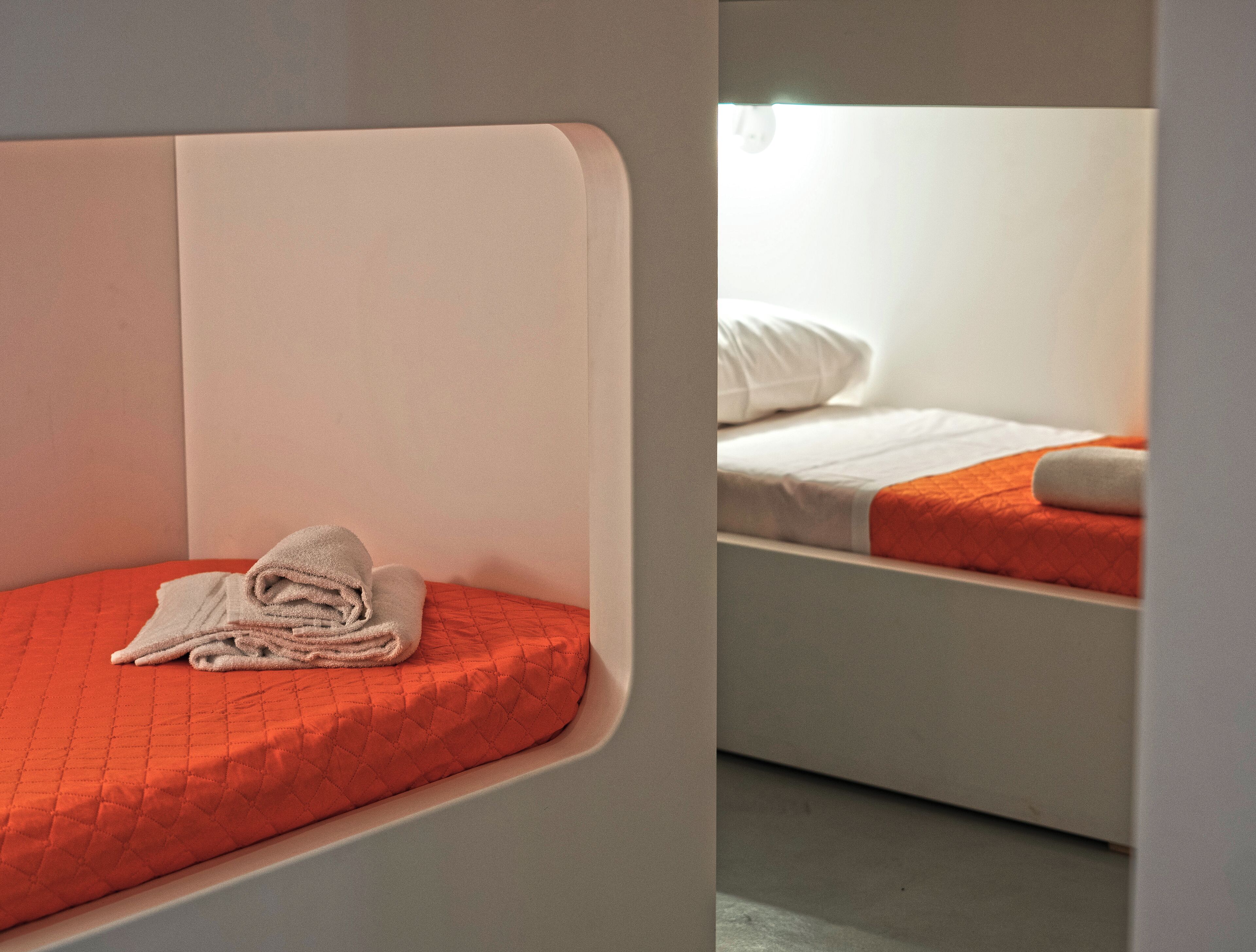 Habitación de hotel con una cama individual, un colchón naranja acolchado y una toalla blanca doblada con cuidado.
